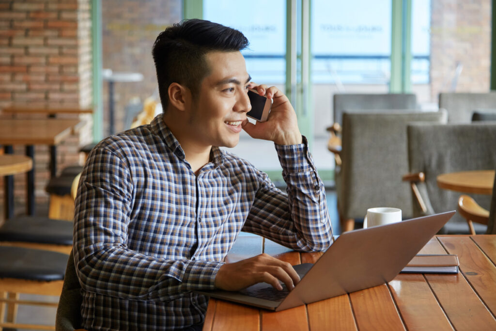 side view asian guy having phone call while working laptop